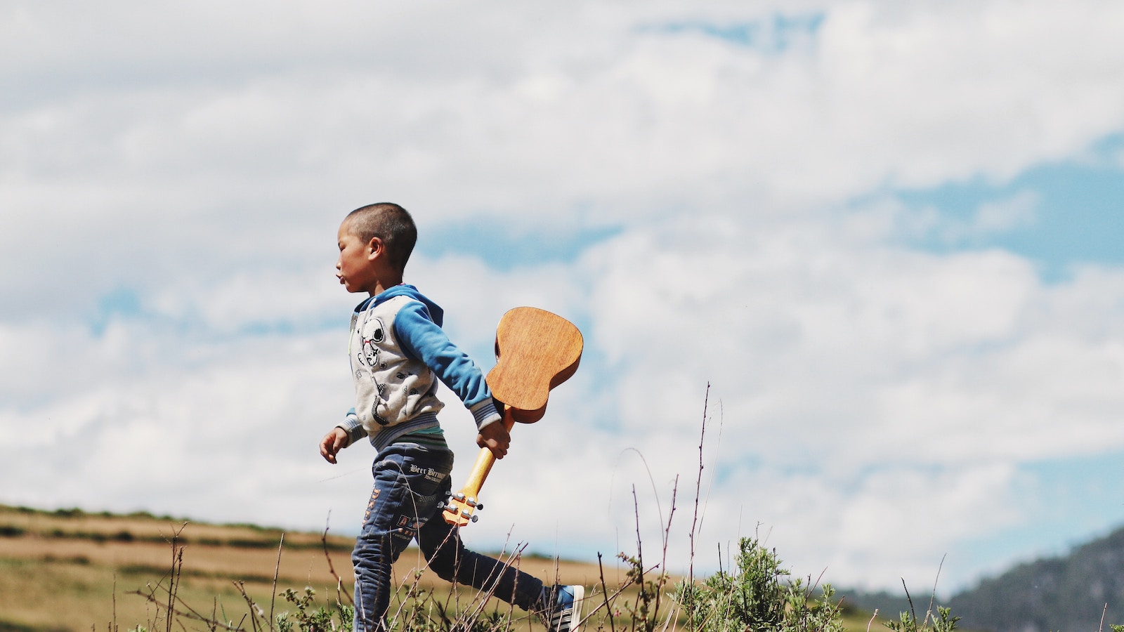 A child in a field with a ukulele, developing character traits for a successful future.